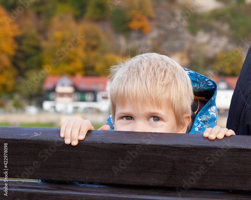 littie blond boy sitting on a bench in park, boy hiding, smiling photo