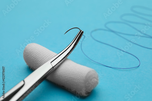 Forceps with suture thread and bandage roll on light blue background, closeup. Medical equipment