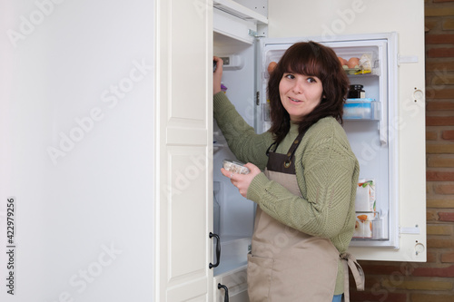 Young woman smiling and opening the fridge to get the ingredients. Cooking time.