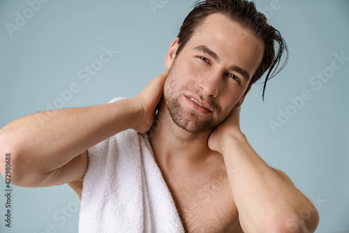 Brunette bearded shirtless man with towel over blue wall