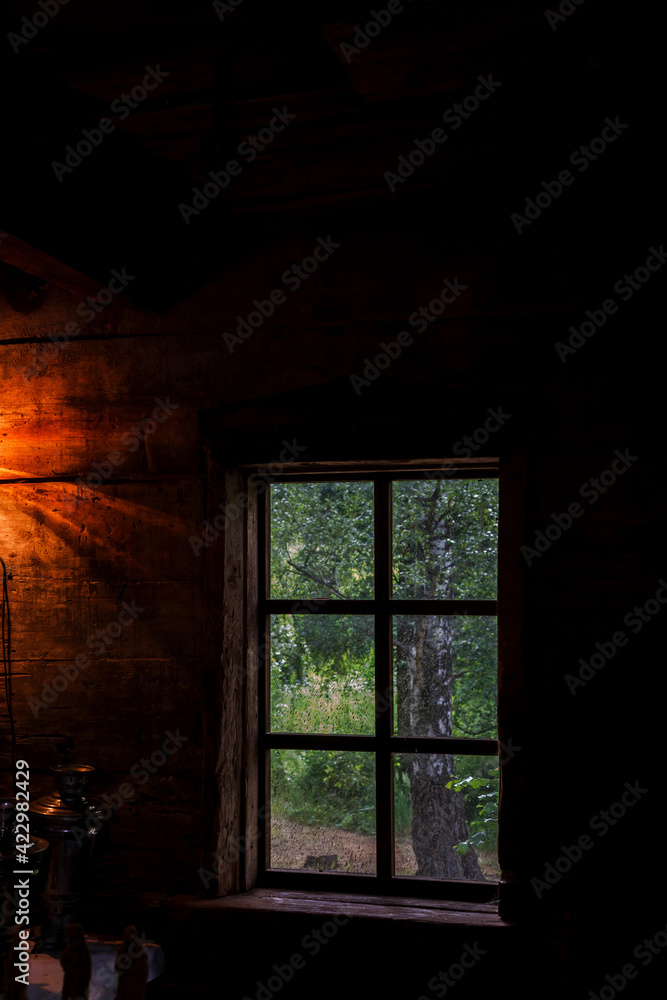 The house is old in the forest. Mysterious mystical fairy light lamp in the scary darkness of the room and a view through the window on a green birch forest