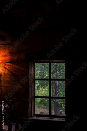The house is old in the forest. Mysterious mystical fairy light lamp in the scary darkness of the room and a view through the window on a green birch forest