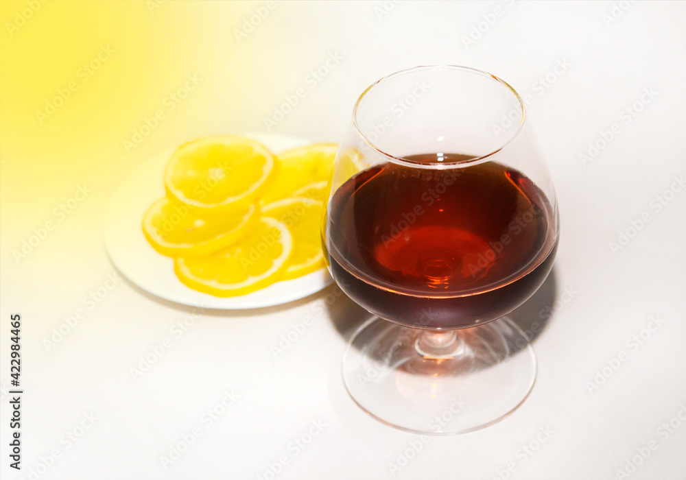 Cognac in a glass next to sliced lemon wedges on a plate. Alcohol and snacks concept Cognac in a glass next to sliced lemon wedges on a plate. Alcohol and snacks concept