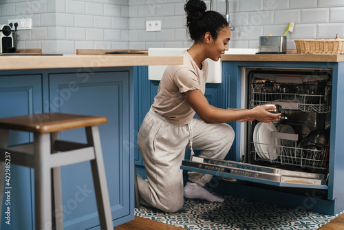 Happy black woman smiling while using dishwasher at home kitchen photo