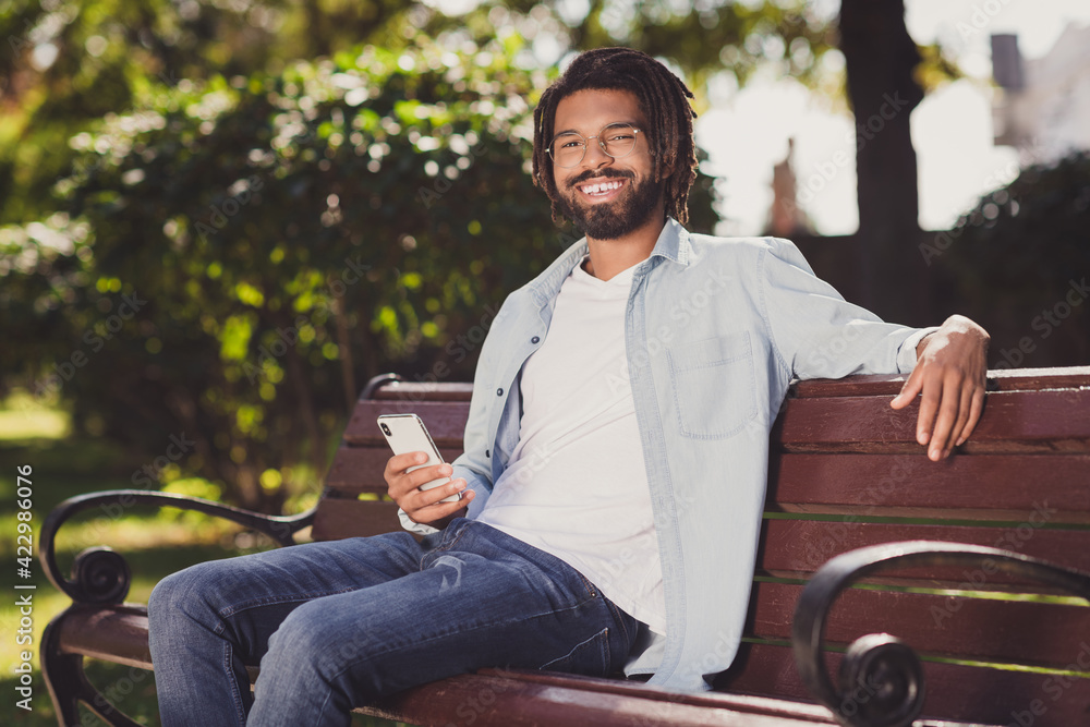 Obraz premium Portrait of attractive cheerful guy sitting on bench using gadget spending free time urban sunny day outside outdoor