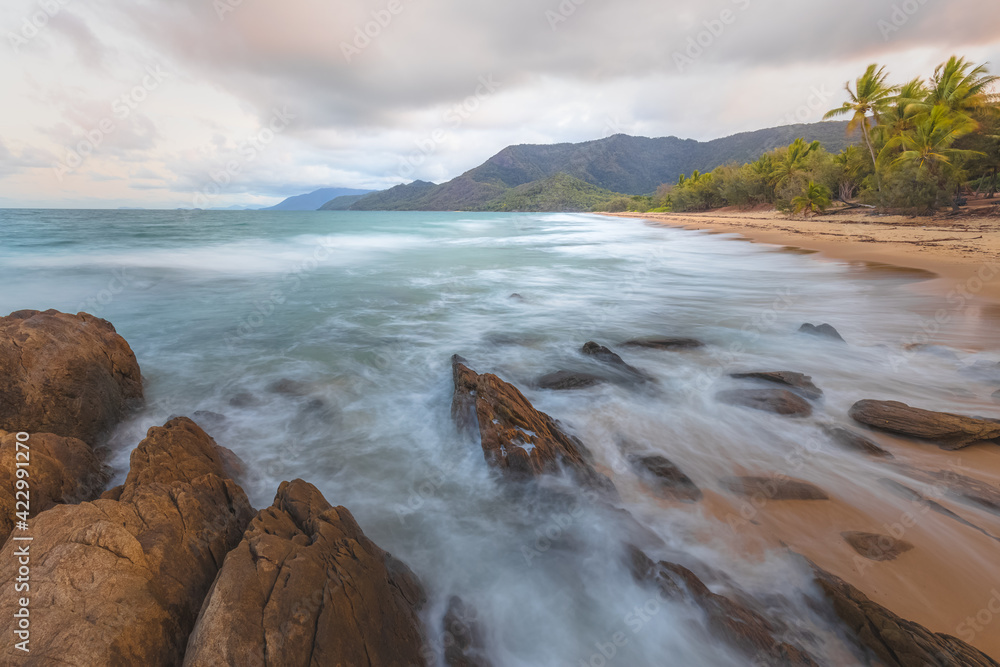 Fototapeta premium Rocky shoreline on an idyllic, tropical sandy Thala Beach near Oak Beach at sunrise or sunset outside Port Douglas and the Daintree in Queensland, Australia.