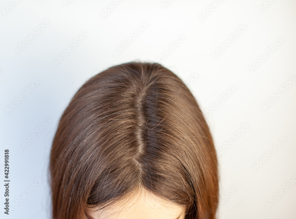 A woman's head with a parting of gray hair that has grown roots due to quarantine. Brown hair on a woman's head close-up. A woman's head with a parting of gray hair that has grown roots due to quarantine. Brown hair on a woman's head close-up.