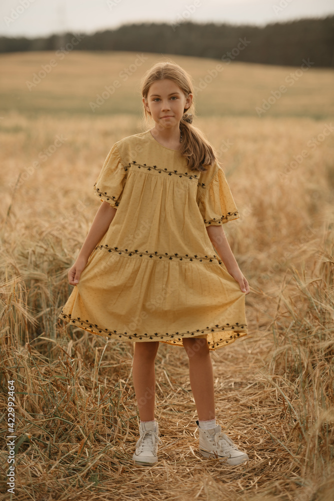 A full-length portrait of a smiling young girl in a dress on the path in the center of the rye field at sunset. A full-length portrait of a smiling young girl in a dress on the path in the center of the rye field at sunset.