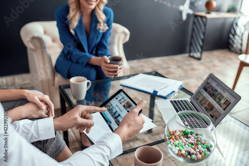 Close up shot of male client holding tablet pc while planning summer vacation with his wife, sitting in modern travel agency office