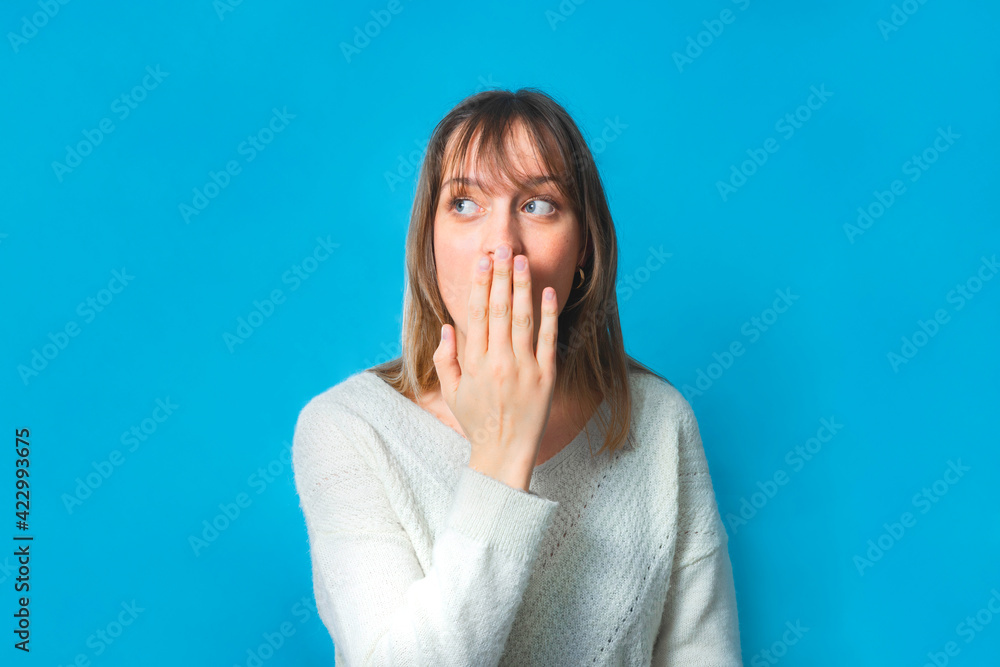 Fun portrait of a charming young woman. The background is blue. She is looking to her side and has piercing blue-eyes. She is shocked, she looks playful and happy. Fun portrait of a charming young woman. The background is blue. She is looking to her side and has piercing blue-eyes. She is shocked, she looks playful and happy.