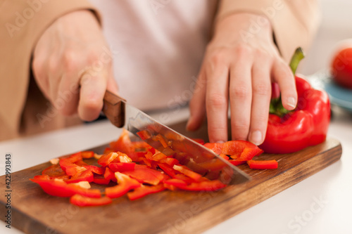 Woman cutting bell pepper on cutting board for salad in kitchen.