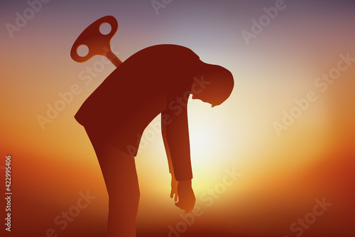 Concept du burnout avec un homme qui tombe d’épuisement faute d’avoir pu recharger ses batteries, symbolisé par une clé planté dans son dos. photo