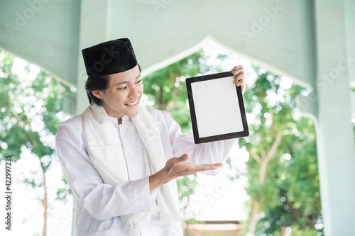 asian man muslim smiling holding and showing blank tablet in mosque