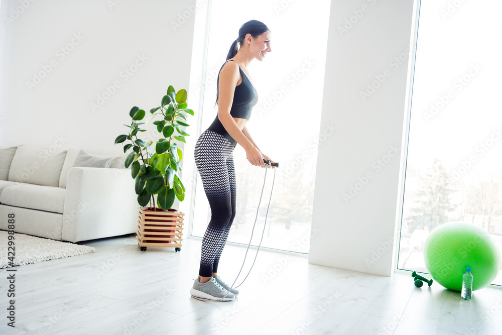 Full size profile side photo of happy good mood smiling cheerful sportive girl training with jump-rope at home house Full size profile side photo of happy good mood smiling cheerful sportive girl training with jump-rope at home house