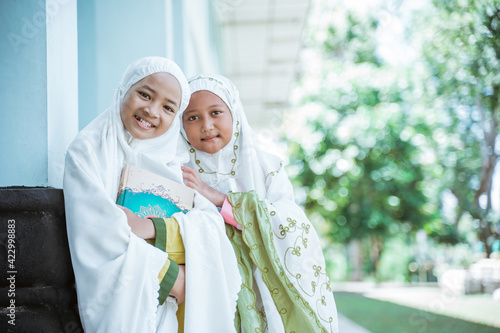 Portrait two Asian Muslim girls wearing mukena holding al quran book after salat together in the mosque photo