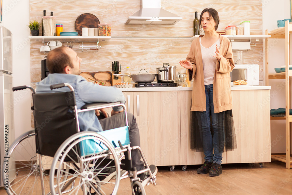 Disabled man in wheelchair having a conflict with wife in kitchen. Disabled paralyzed handicapped man with walking disability integrating after an accident. Disabled man in wheelchair having a conflict with wife in kitchen. Disabled paralyzed handicapped man with walking disability integrating after an accident.