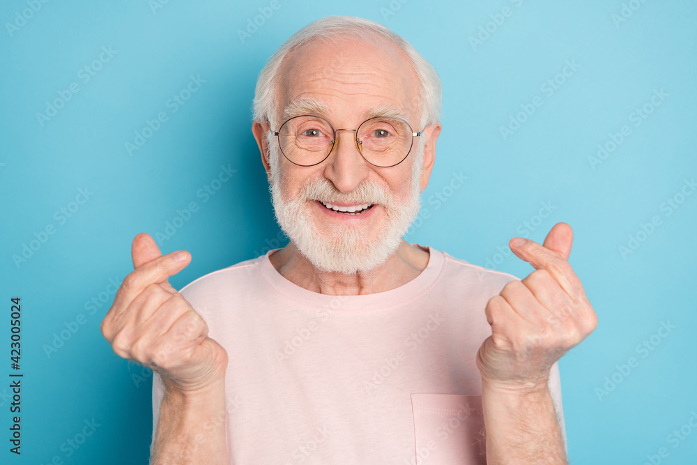Photo of aged man pensioner happy positive smile show finger money cash sign isolated over blue color background Photo of aged man pensioner happy positive smile show finger money cash sign isolated over blue color background