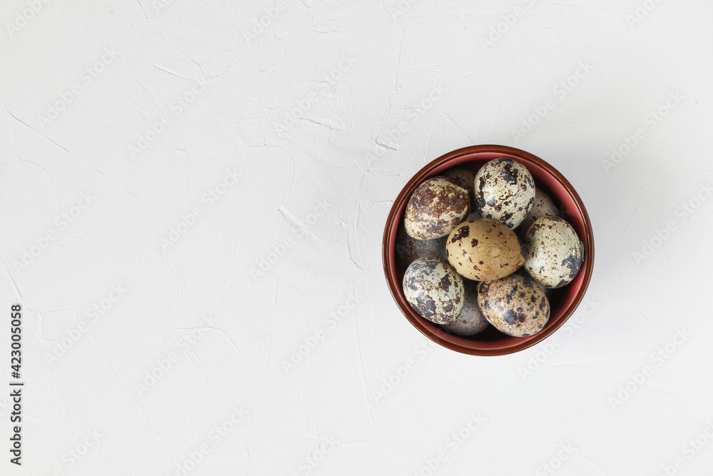 Colorful quail eggs in a bowl on a white table - top view Colorful quail eggs in a bowl on a white table - top view