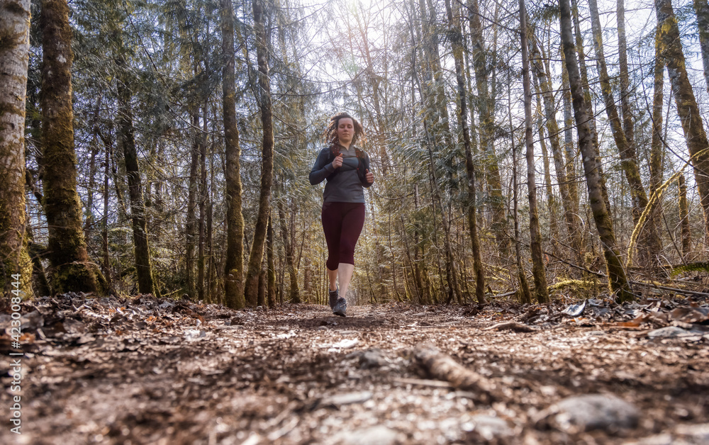 Caucasian Woman Trail Running in the Green Forest surrounded by beautiful trees. Taken in Squamish, British Columbia, Canada. Caucasian Woman Trail Running in the Green Forest surrounded by beautiful trees. Taken in Squamish, British Columbia, Canada.