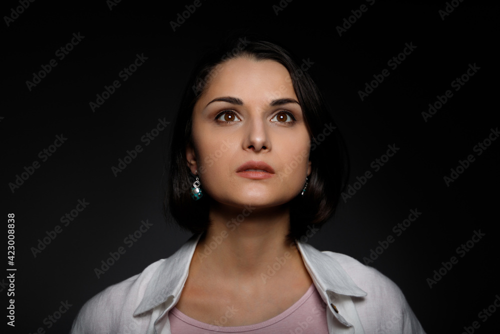 Low key portrait of serious young brunette multiethnic woman in pink tank and white shirt looking up Low key portrait of serious young brunette multiethnic woman in pink tank and white shirt looking up