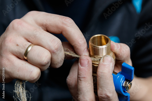 Cloce-up sealing pipe connections with linum flax. Professional plumber sealing threaded ends faucet with flax