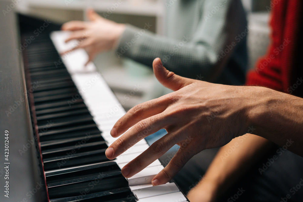 Obraz premium Close-up of unrecognizable child boy playing piano, music teacher sits near and helps with playing during lesson at music school. Kid practicing piano lesson in living room. Concept of music education