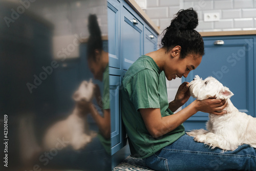 Photography Smiling black woman playing with her dog while sitting on floor