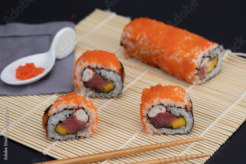 Sushi rolls with salmon avocado tuna and mango in a mat and black background