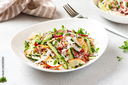 Rice noodle salad with cucumber, apple, onion, sesame seeds, and herbs in a white bowl on a light concrete background. Vegan salad Asian style. Vegetarian food. Vegetable salad with rice noodles