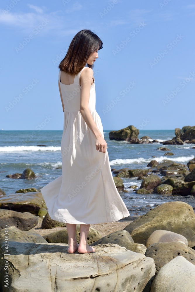 海岸でポーズをとる白いワンピース姿の若い女性 Stock Foto Adobe Stock