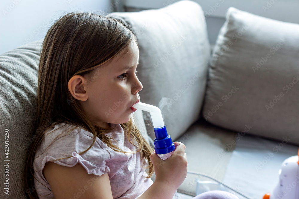 Beautiful girl uses a nebulizer at home, treatment of bronchitis and asthma with inhalation. Caucasian child holding oxygen or inhaler mask at home. Girl does therapeutic inhalation using a nebulizer. Beautiful girl uses a nebulizer at home, treatment of bronchitis and asthma with inhalation. Caucasian child holding oxygen or inhaler mask at home. Girl does therapeutic inhalation using a nebulizer.