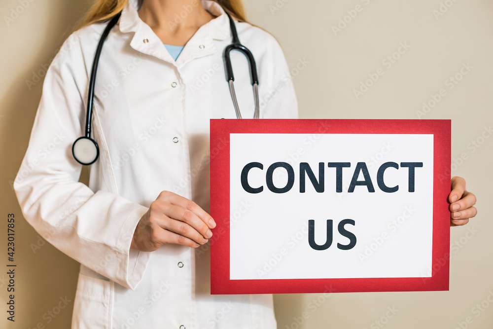 Image of female doctor holding a paper with a text contact us. Image of female doctor holding a paper with a text contact us.