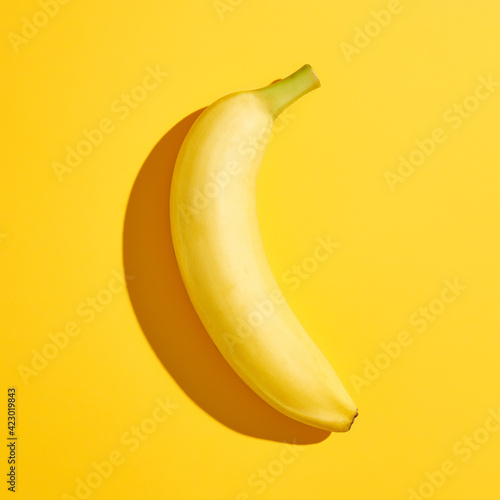 Banana with hard shadow on yellow background, from above