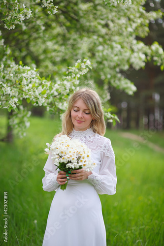 beautiful girl  a blonde in a vintage white dress walks in a blooming apple orchard  a bouquet of anemones  a bride
