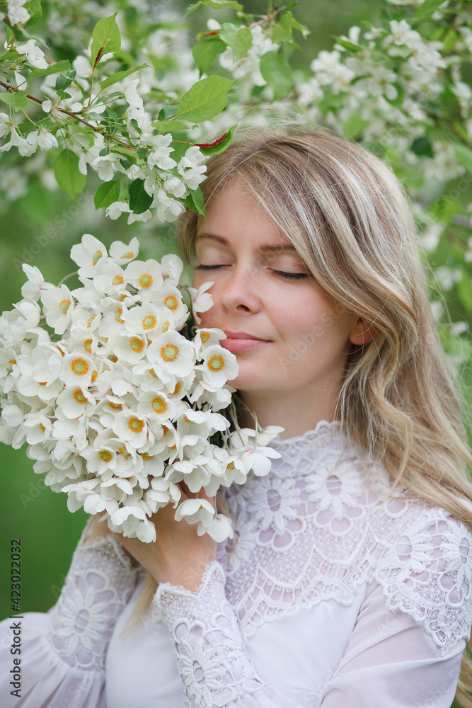 Fototapeta premium beautiful girl, a blonde in a vintage white dress walks in a blooming apple orchard, a bouquet of anemones, a bride