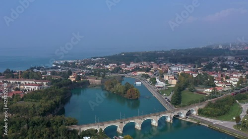 Point of interest behind the movement of the train. Top view of the movement of a red train on an arched bridge over a mountain river. Panoramic view of Lake Garda, Italy.  photo