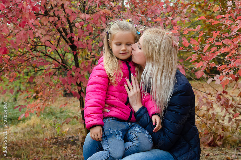 A little girl walks and plays with her mother in the park. Autumn landscape with golden leaves A little girl walks and plays with her mother in the park. Autumn landscape with golden leaves