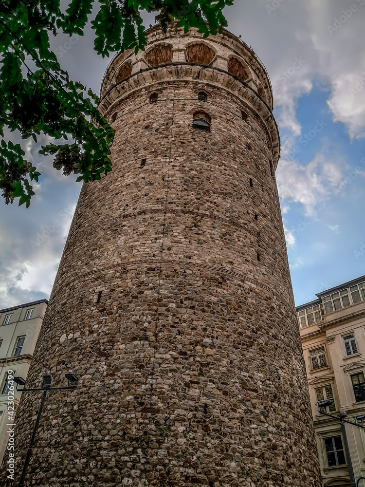 Bottom view of Galata Tower in Istanbul (Turkey), close-up. Ancient tall round stone building on cloudy sky background, vertical
