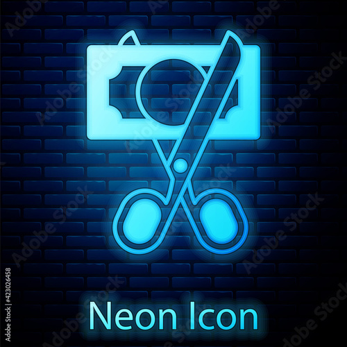 Glowing neon Scissors cutting money icon isolated on brick wall background. Price, cost reduction or price reduction icon concept. Vector