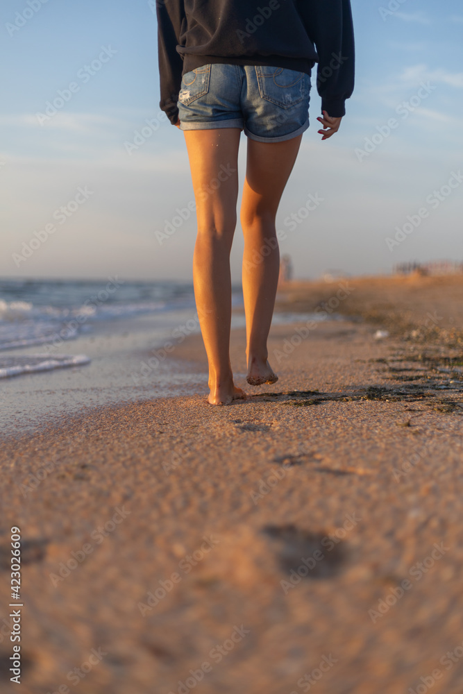 Naklejka premium traces of female steps in the sand. girl walks in short shorts on the beach