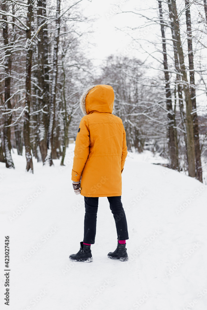 Caucasian woman in an orange jacket in the winter woods, jumping and having fun, enjoying the beauty of nature and enjoying life