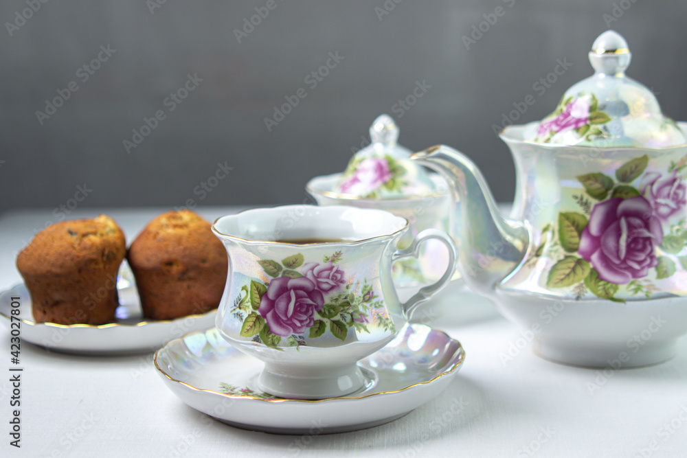 A cup of tea on a white tablecloth. Tea with muffins. Light breakfast. White tea set with flowers. A cup of tea on a white tablecloth. Tea with muffins. Light breakfast. White tea set with flowers.
