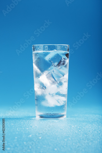 A glass with ice water and ice cubes on a blue background.