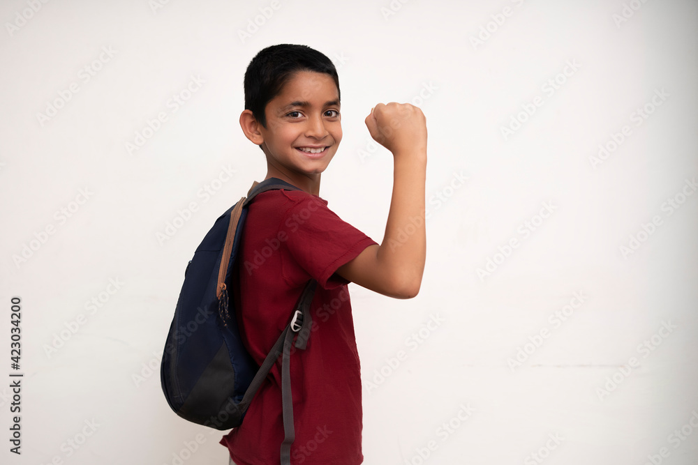 Banner image of an indian happy kid going to school with his bag on his back and showing his arms on a white wall with copy space. Banner image of an indian happy kid going to school with his bag on his back and showing his arms on a white wall with copy space.