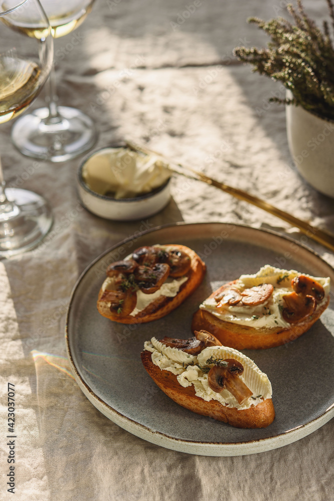 Bruschettas or toasts with cheese and fried mushrooms with thyme served with glasses of wine on greige linen tablecloth Bruschettas or toasts with cheese and fried mushrooms with thyme served with glasses of wine on greige linen tablecloth