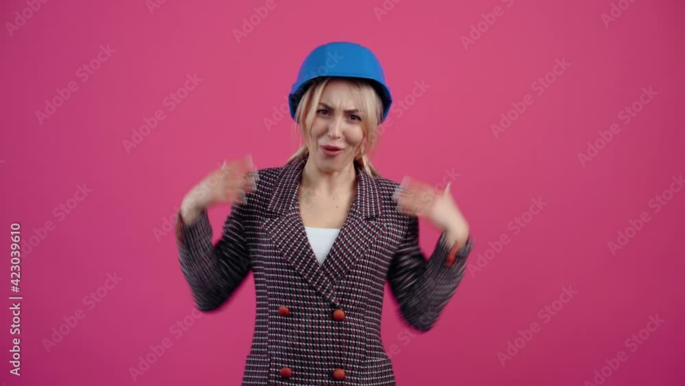 Mature blonde with engineer helmet on blue collar head, smiles wide looking into the room young mature blonde in pink jacket. Mature blonde with engineer helmet on blue collar head, smiles wide looking into the room young mature blonde in pink jacket.
