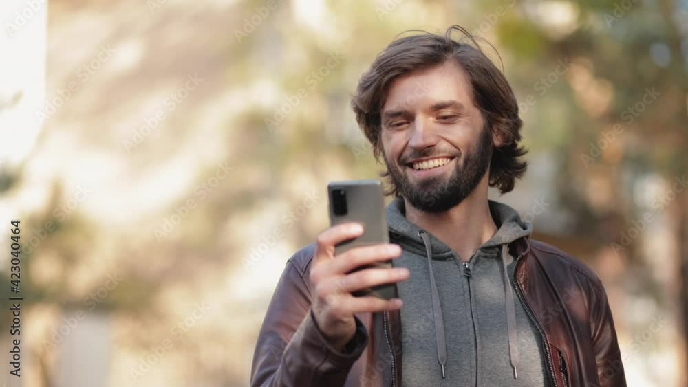 Positive Bearded Man standing on the Street Receiving Funny Message on Phone. Happy Male spending Free time Outdoors using Smartphone, Browsing on Social Media. Enjoys online communication. Chatting. Positive Bearded Man standing on the Street Receiving Funny Message on Phone. Happy Male spending Free time Outdoors using Smartphone, Browsing on Social Media. Enjoys online communication. Chatting.