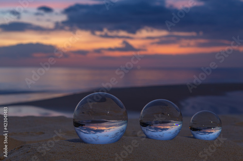 Three clear crystal balls of three sizes are sphere reveals  seascape view with spherical .placed on the sand at Karon Beach during sunset. © Narong Niemhom
