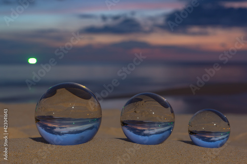 Three clear crystal balls of three sizes are sphere reveals  seascape view with spherical .placed on the sand at Karon Beach during sunset. © Narong Niemhom