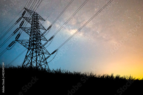 The silhouette of the high voltage transmission tower has a complex steel structure. High voltage pole silhouette In the meadow there is a background of the night sky and the milky way.